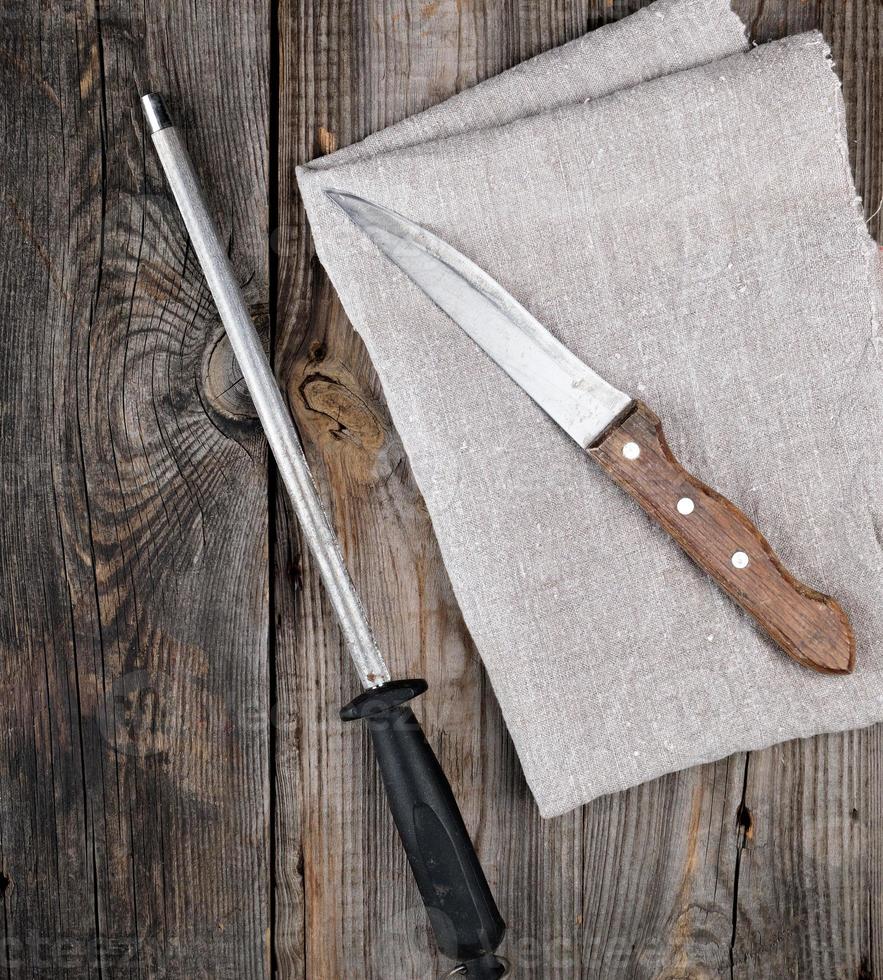 old sharp knife and sharpener with a handle on a gray wooden background photo