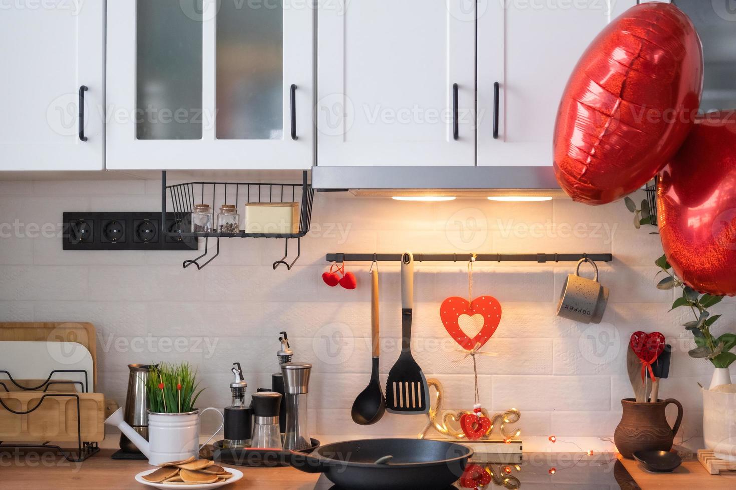 el interior de la cocina de la casa está decorado con corazones rojos para el día de san valentín. decoración en la mesa, estufa, utensilios, ambiente festivo en un nido familiar foto