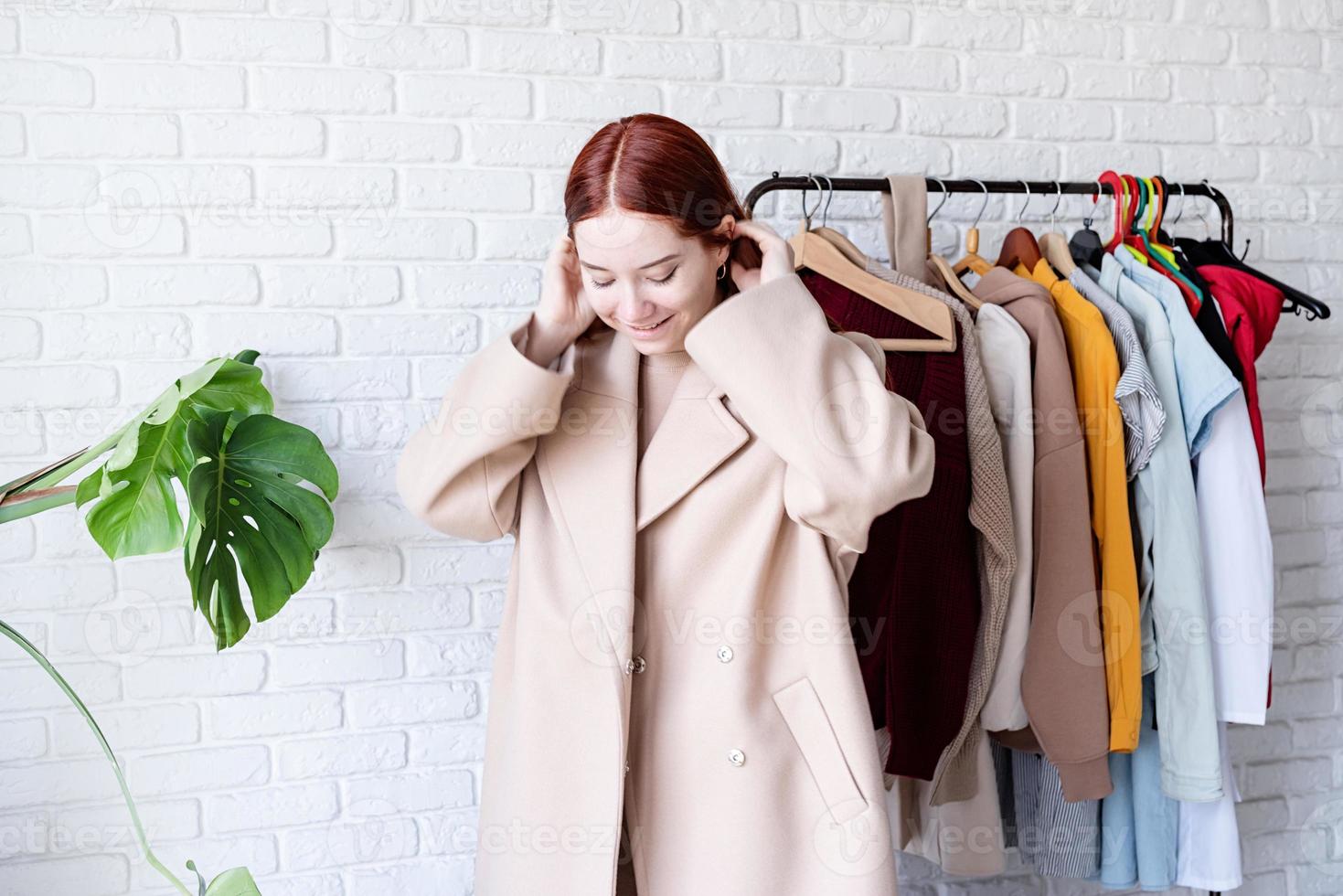 young beautiful woman wearing beige pastel coat, standing near clothes rack. Wardrobe change photo