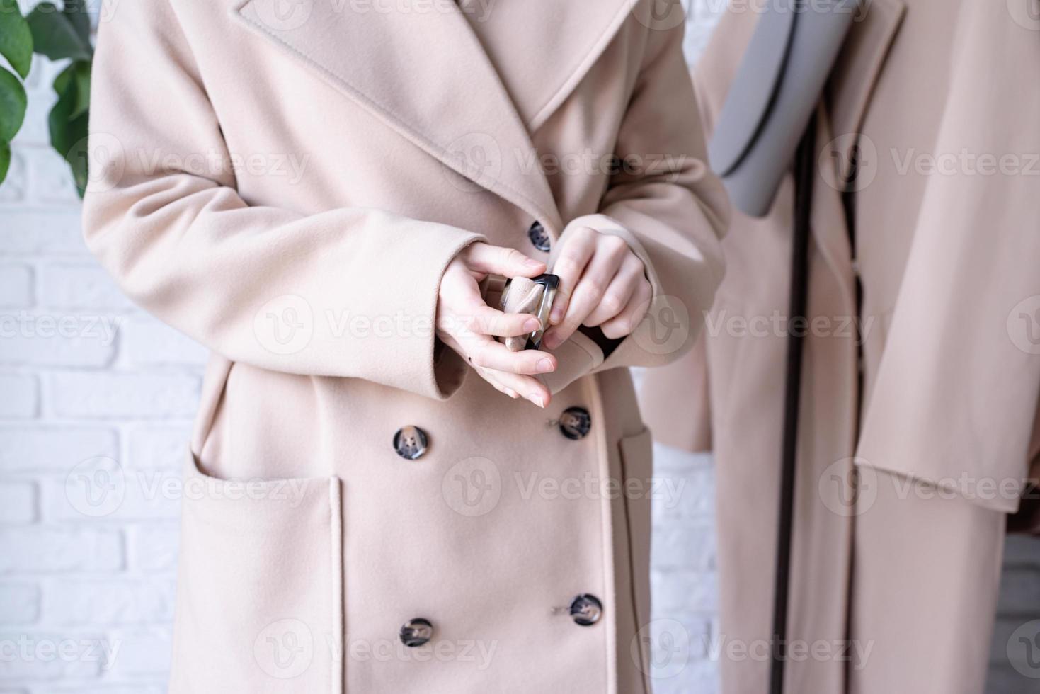 mujer vistiendo beige pastel abrigo, en pie cerca ropa estante. guardarropa cambio foto