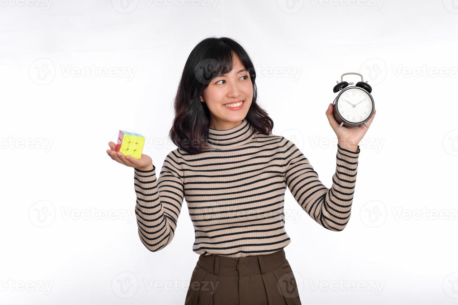 Asian woman holding alarm clock and rubik cube standing on white background. solving cubic problems, problem solution and making strategic moves concept photo