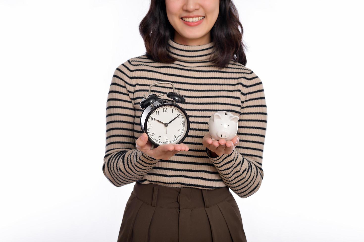Happy Asian woman with sweater shirt holding alarm clock and piggy bank isolated on white background photo