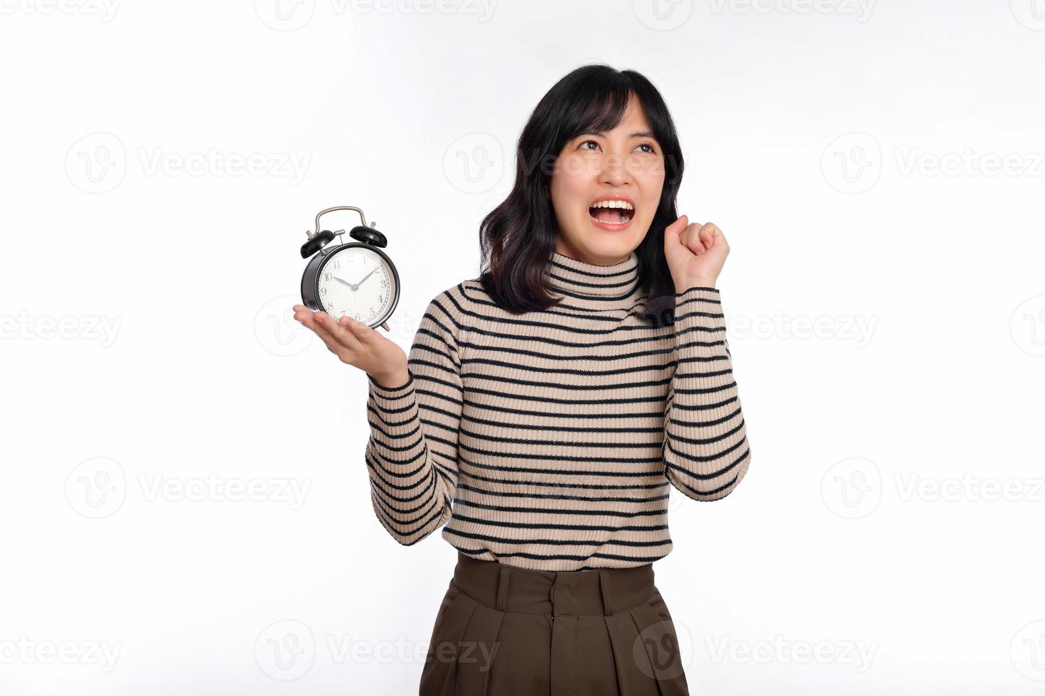 Portrait of excited young Asian woman with sweater shirt holding alarm clock isolated on white background photo