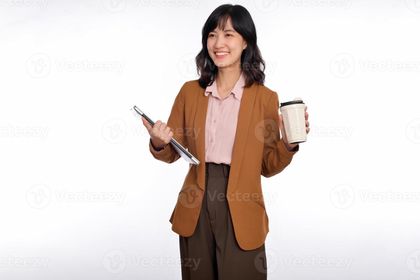 hermosa sonriente joven asiático mujer de negocios que lleva ordenador portátil computadora y taza de café a Vamos mientras en pie aislado terminado blanco antecedentes foto