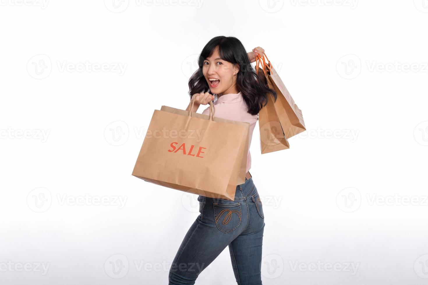 joven contento asiático mujer con casual camisa y mezclilla pantalones participación compras papel bolso aislado en blanco antecedentes foto