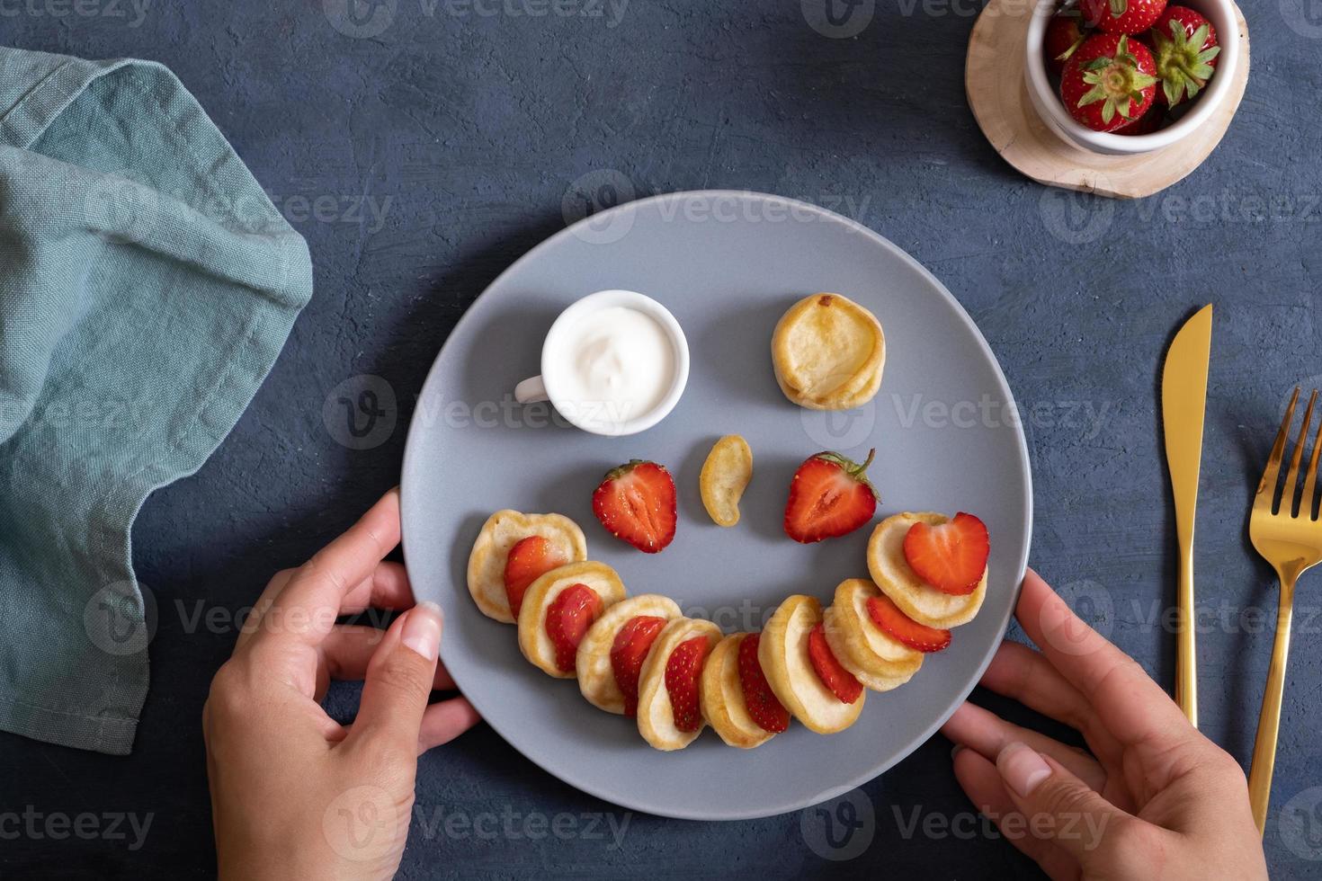 Small pancakes with strawberries in the original serving in the form of a smiley face. Top view. Flat lay photo