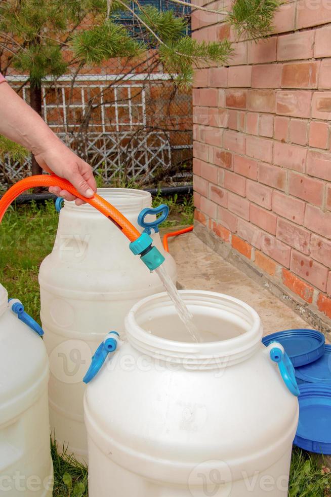 A woman's hand fills a plastic barrel with water from a hose. The concept of the drinking water crisis in the world. photo