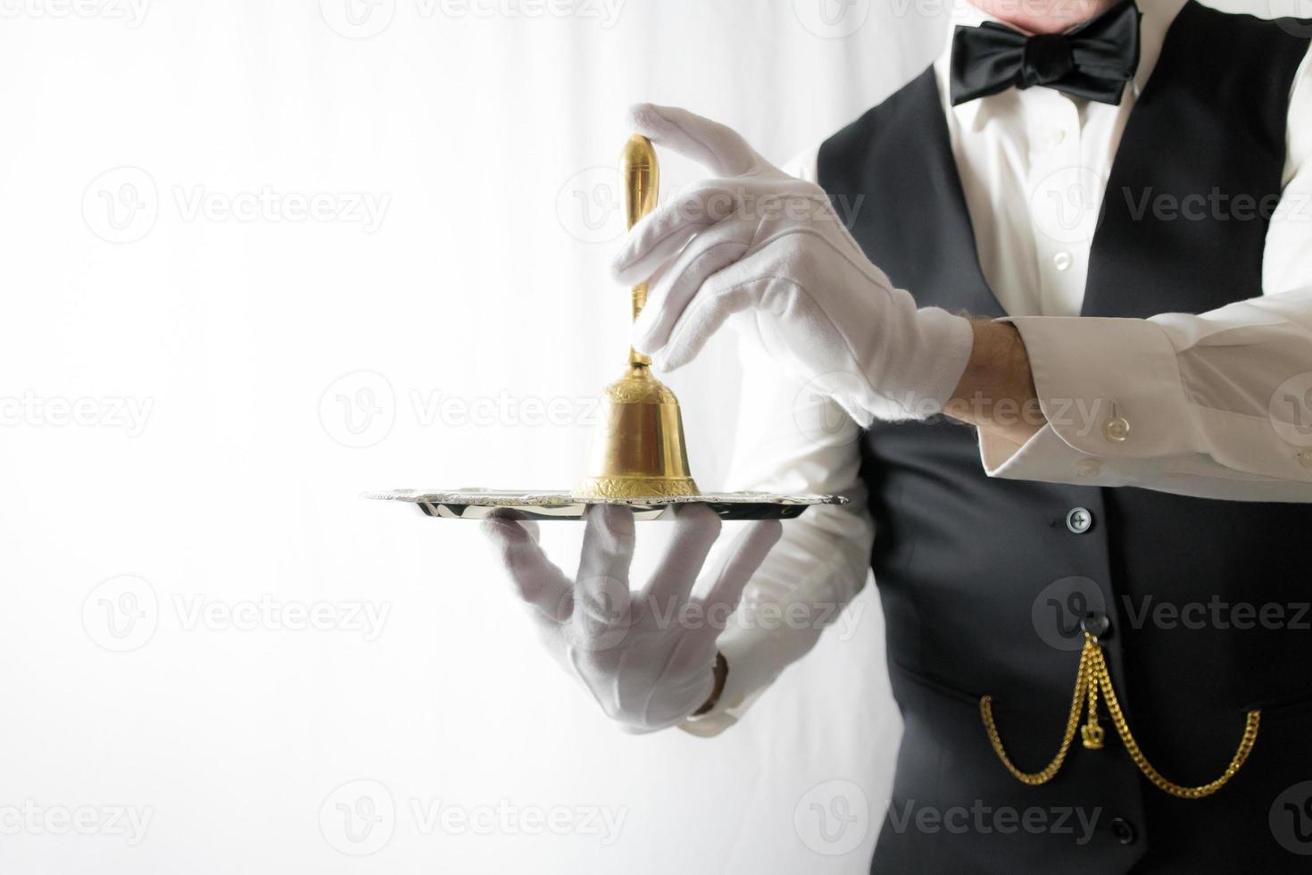 Butler or Waiter in Black Vest and White Gloves Holding Gold Bell on Silver Serving Tray. Concept of Service Industry and Professional Hospitality. photo