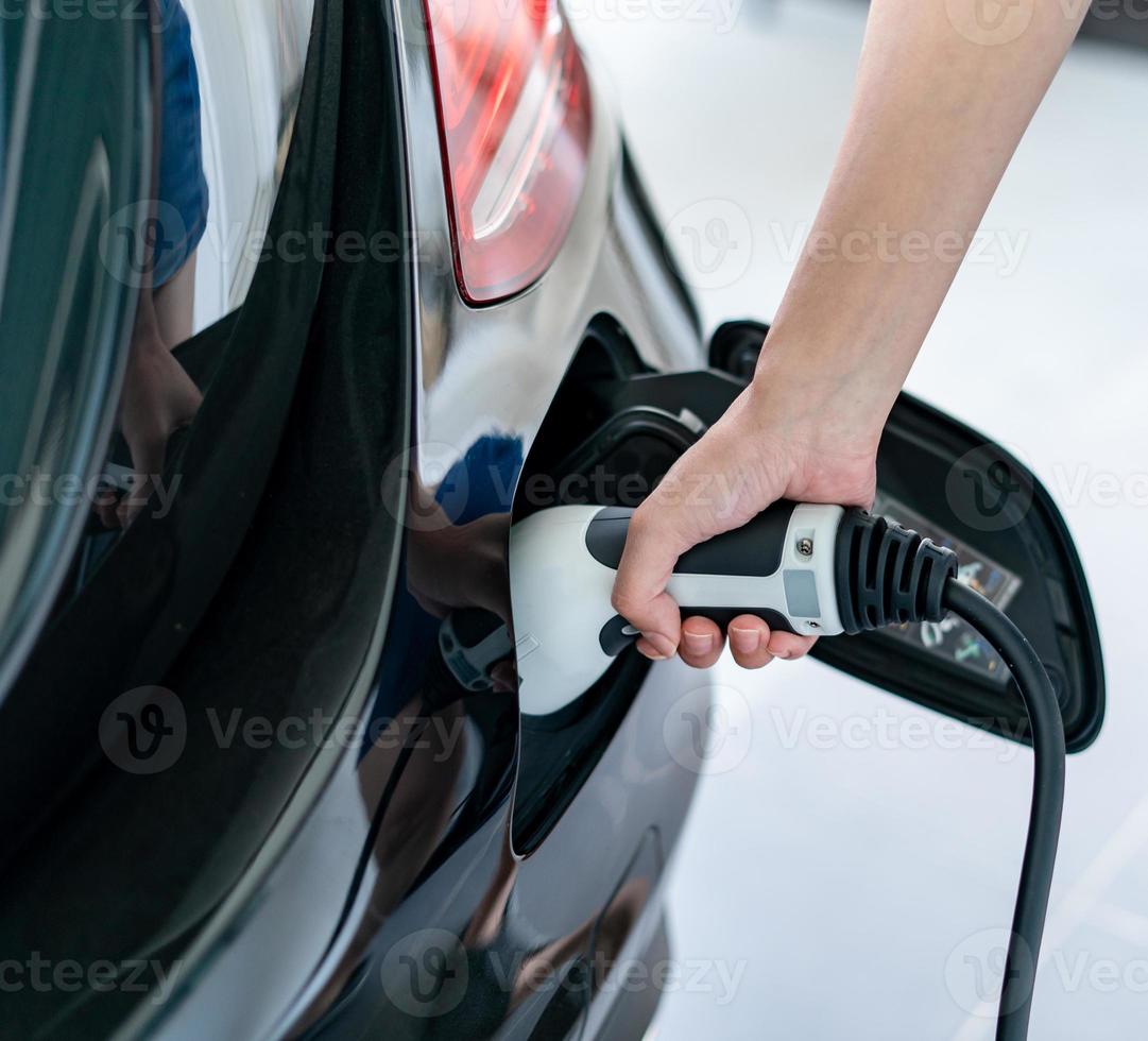 mujer atascado cable cargando un eléctrico coche a hogar. foto