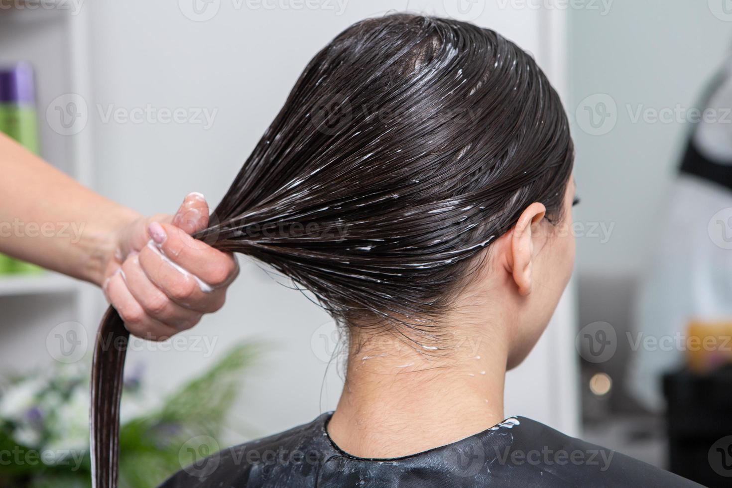 Hairdresser applies a hair mask to straight black hair. Hair care at the beauty salon. photo