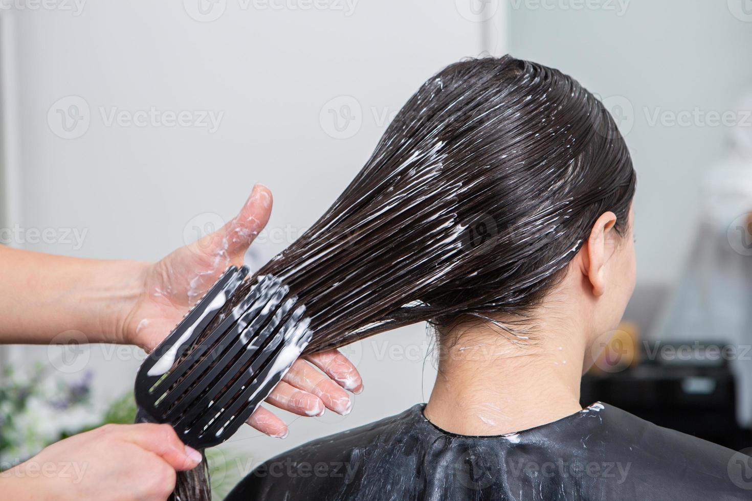 Hairdresser applies a hair mask to straight black hair. Hair care at the beauty salon. photo