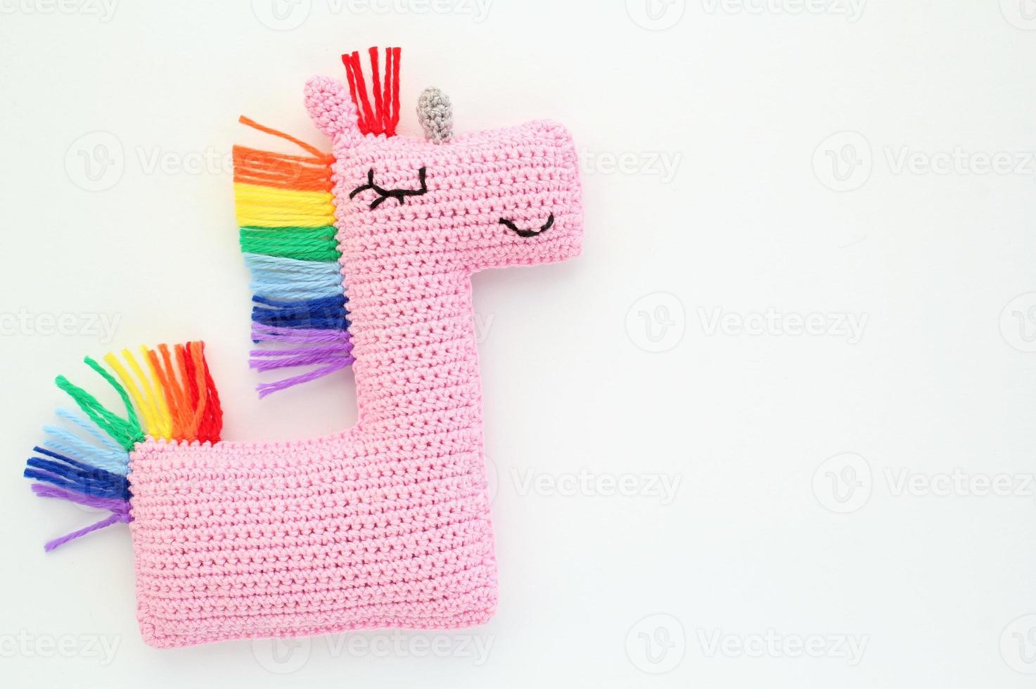 Crochet amigurumi handmade stuffed soft pink unicorn toy with rainbow mane on white background. Handwork, hobby. Craft diy newborn pregnancy concept. Knitted doll for little baby. Close up flat lay photo