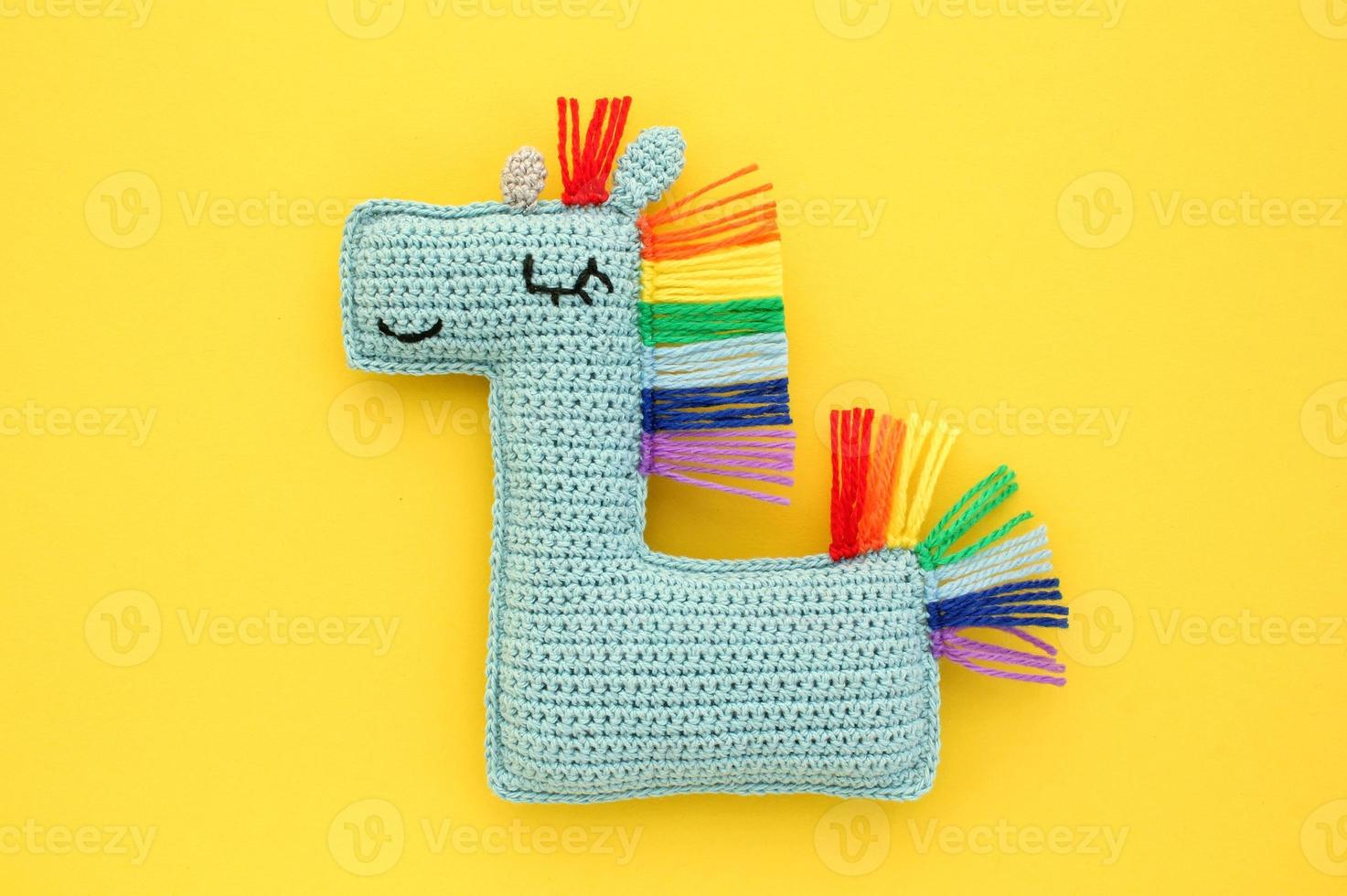 Crochet amigurumi handmade stuffed soft blue unicorn toy with rainbow mane on yellow background. Handwork, hobby. Craft diy newborn pregnancy concept. Knitted doll for little baby. Close up flat lay photo