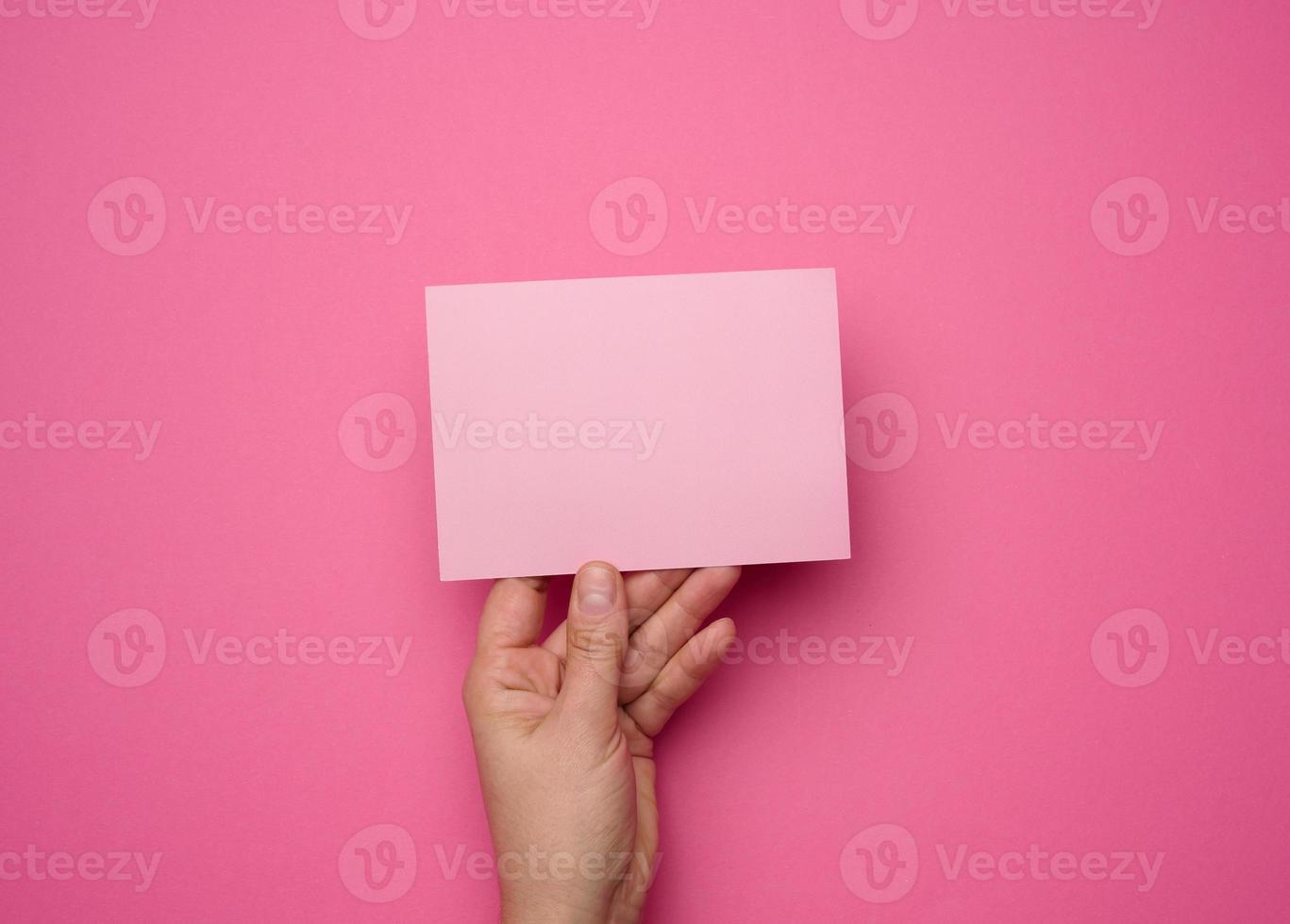 Female hand holding empty pink paper on a pink background. Copy paste image or text, close up photo