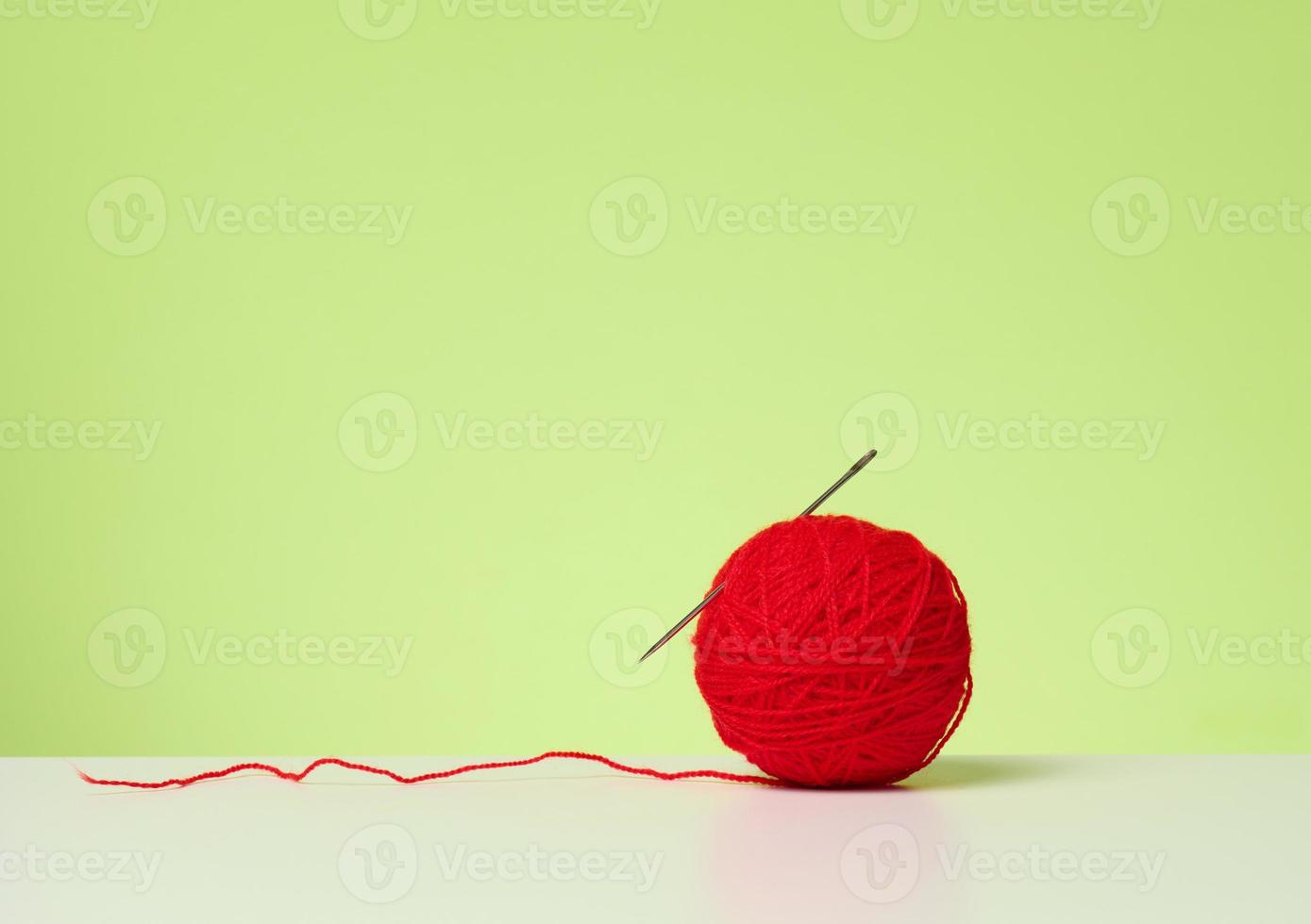 red ball with woolen thread on white table, green background photo
