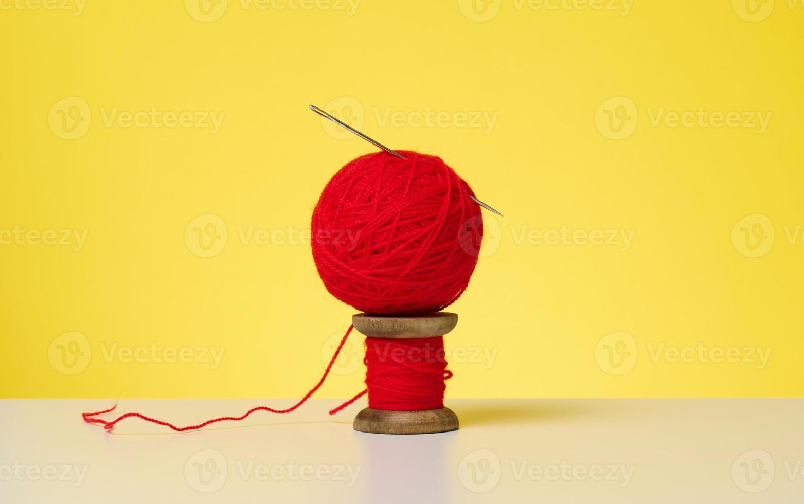 wooden spool with red wool thread and a large needle on a white table. Handicraft items photo