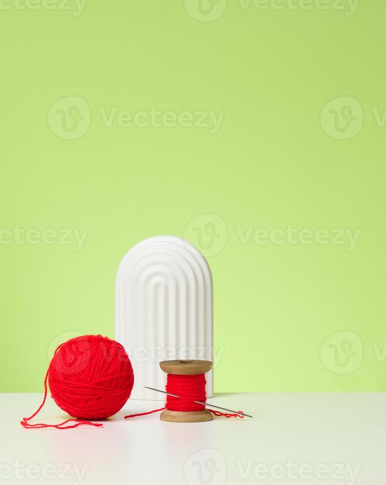red ball with woolen thread and large needle on white table, green background photo