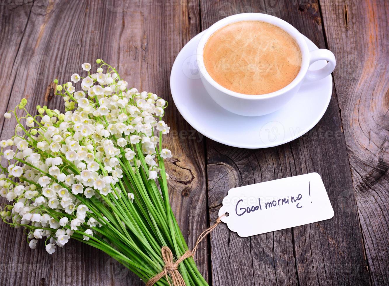 cup of hot black coffee and a bouquet of fresh lilies of the valley on a gray wooden surface photo