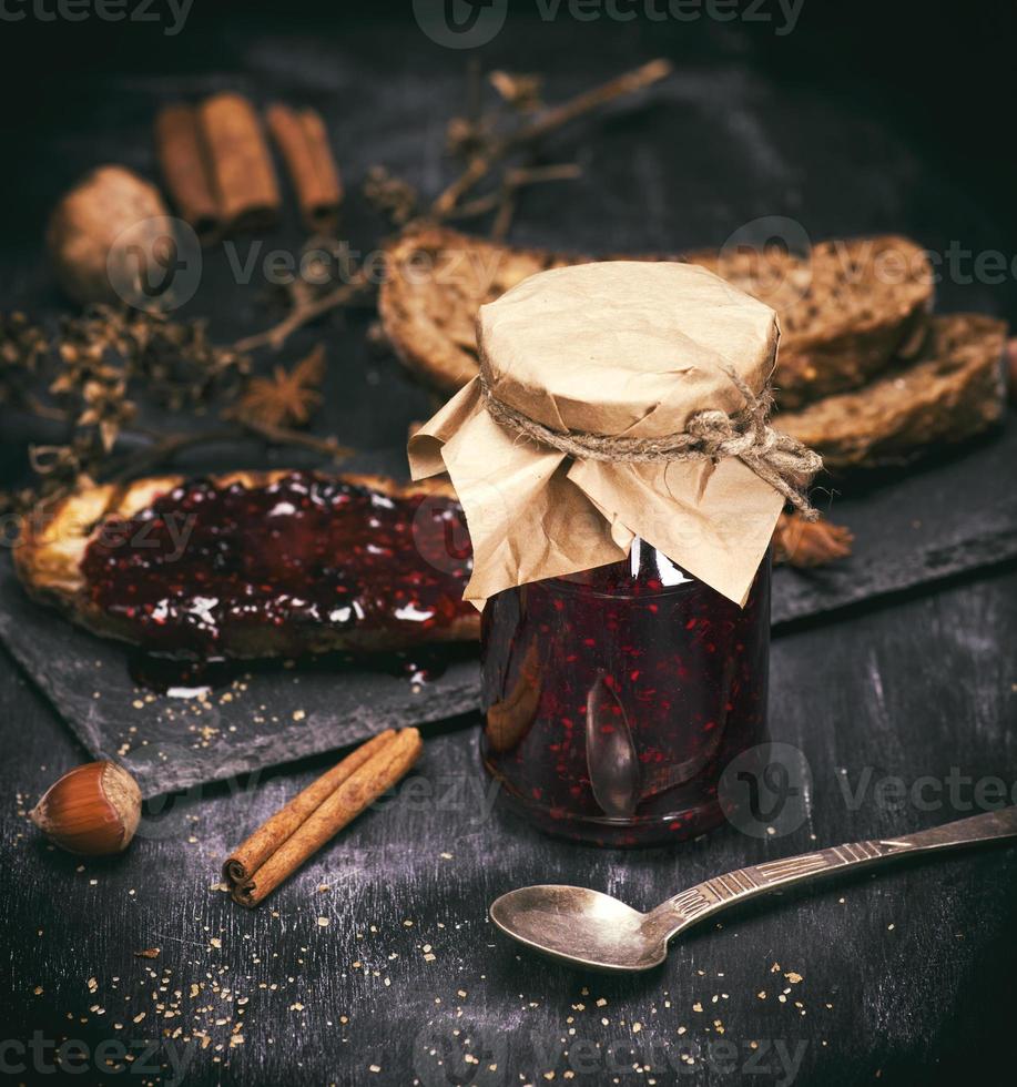 raspberry jam in a glass jar next to an iron spoon photo