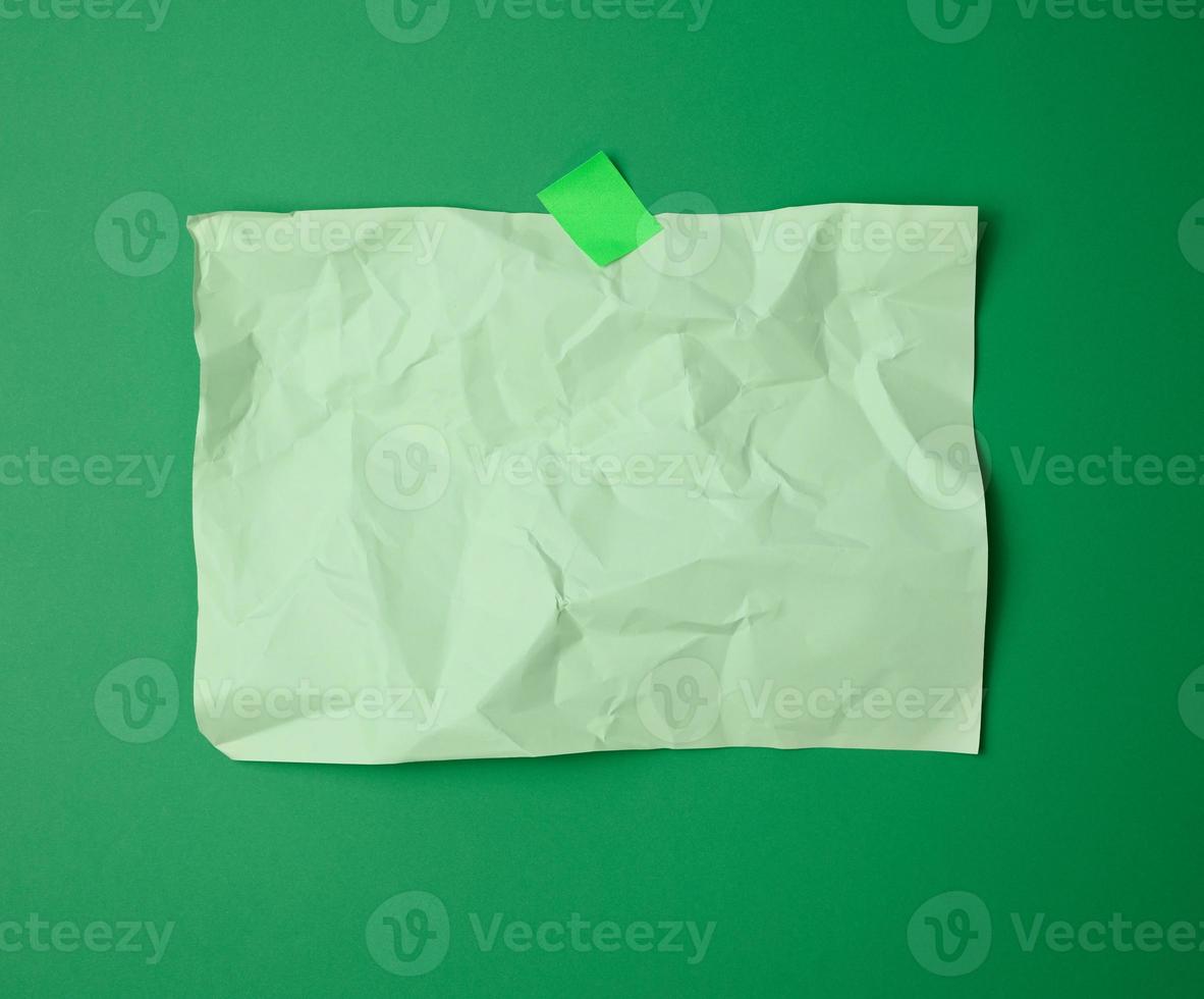rectangular crumpled blank green sheet of paper glued with green sticky paper on green background photo