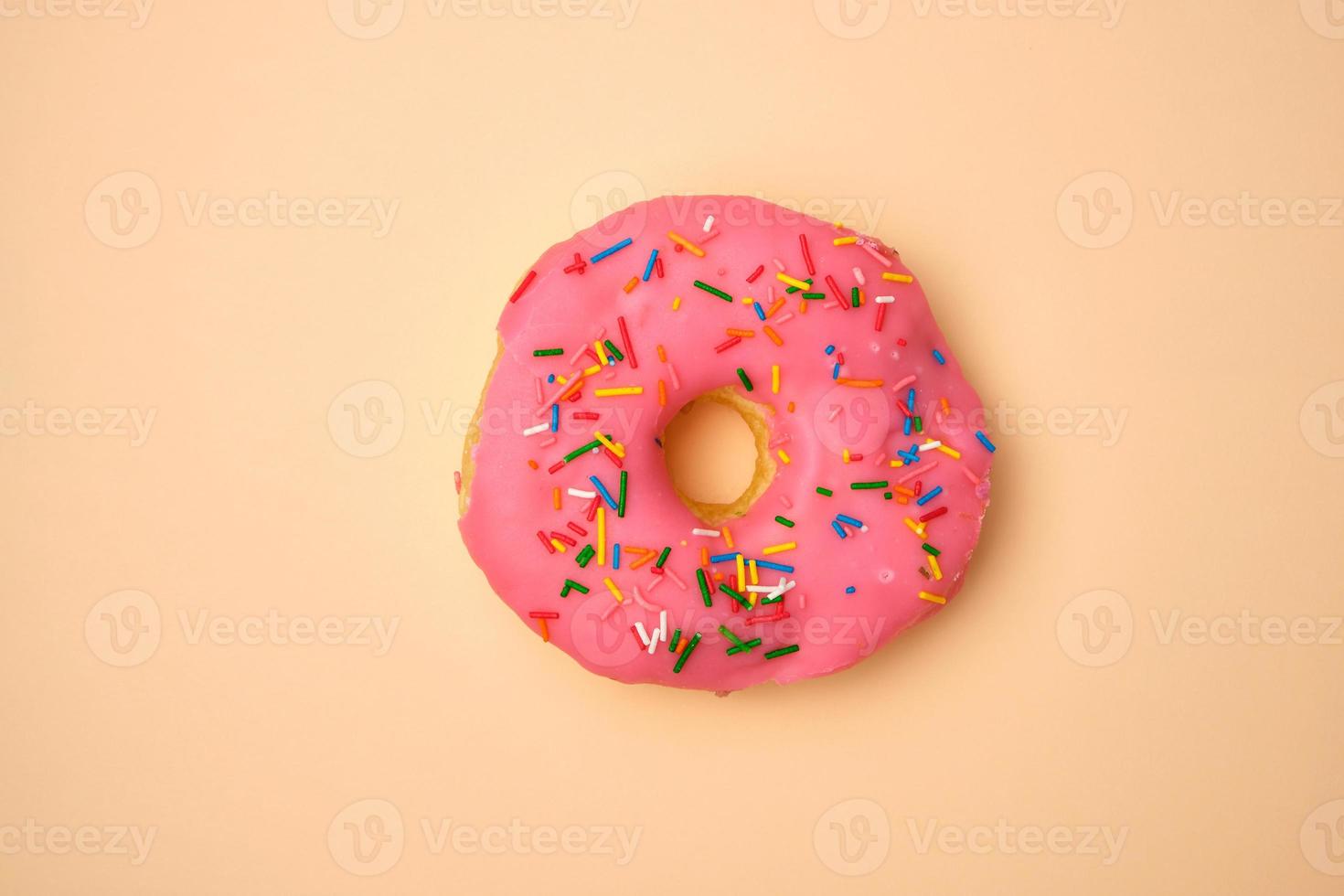 pink round donut with colored sprinkles on a beige background photo
