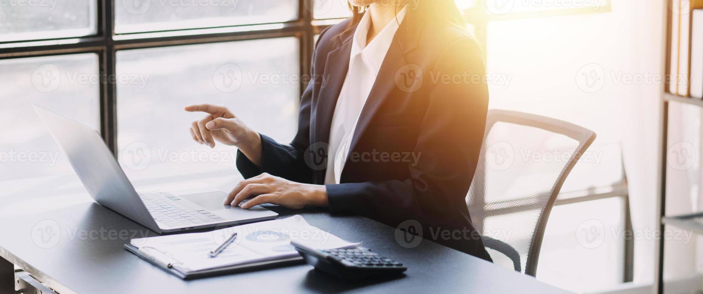 Asian Business woman using calculator and laptop for doing math finance on an office desk, tax, report, accounting, statistics, and analytical research concept photo