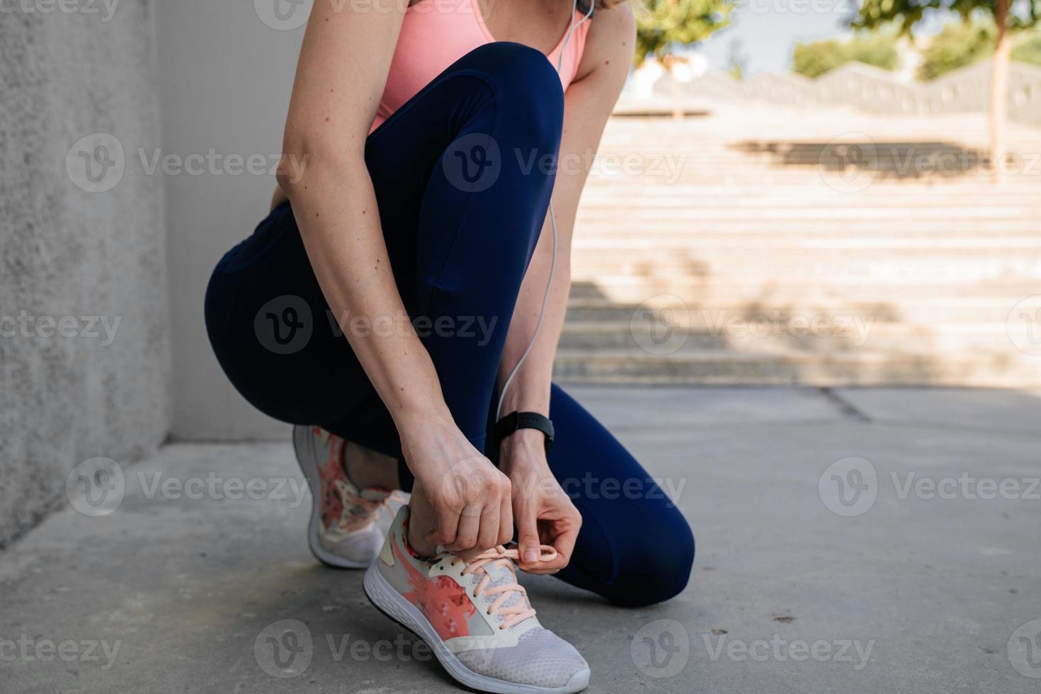 Sporty girl tying shoelaces near the wall in headphones photo