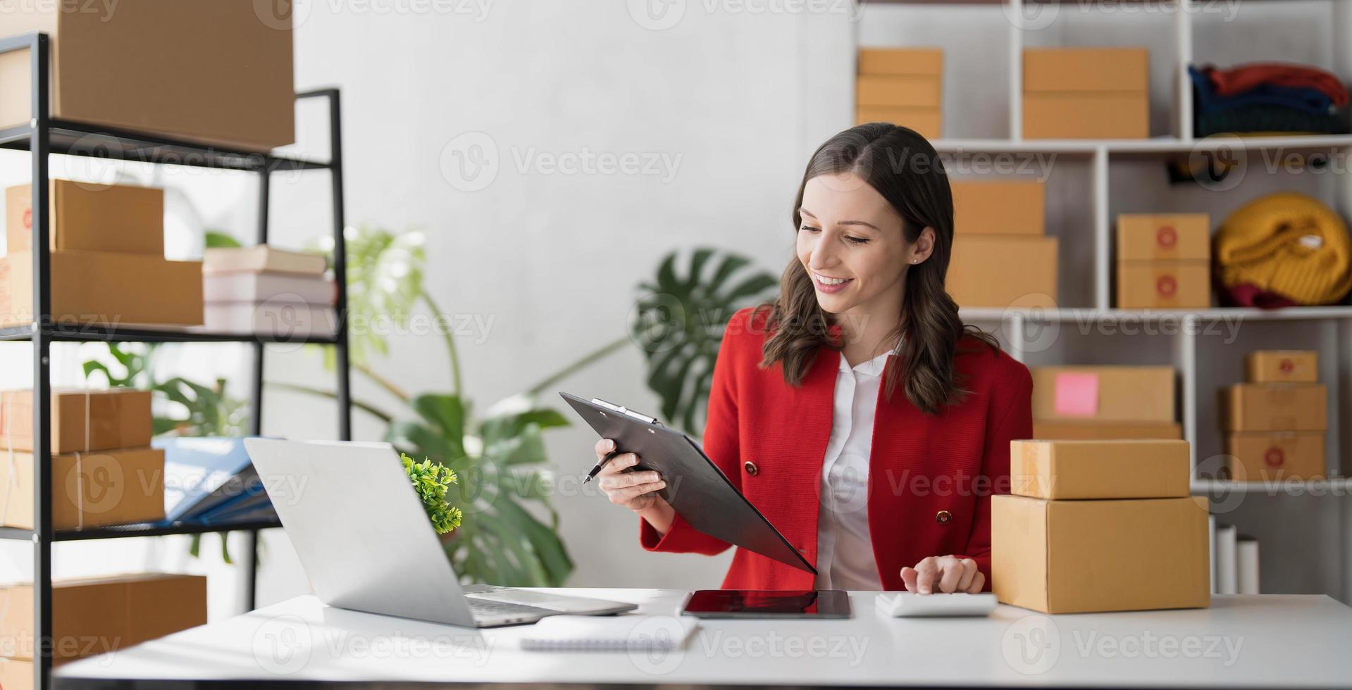 Entrepreneur using calculator with pencil in her hand, calculating financial expense at home office,online market packing box delivery,Startup successful small business owner, SME, concept photo