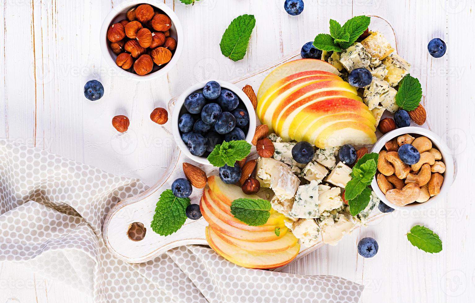 Cheese platter with assorted cheeses, blueberry, apples, nuts on white table. Italian cheese  platter and fruit. Top view, overhead photo