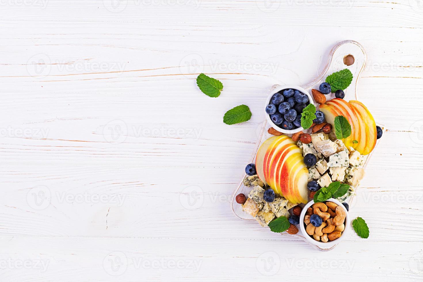 Cheese platter with assorted cheeses, blueberry, apples, nuts on white table. Italian cheese  platter and fruit. Top view, overhead photo