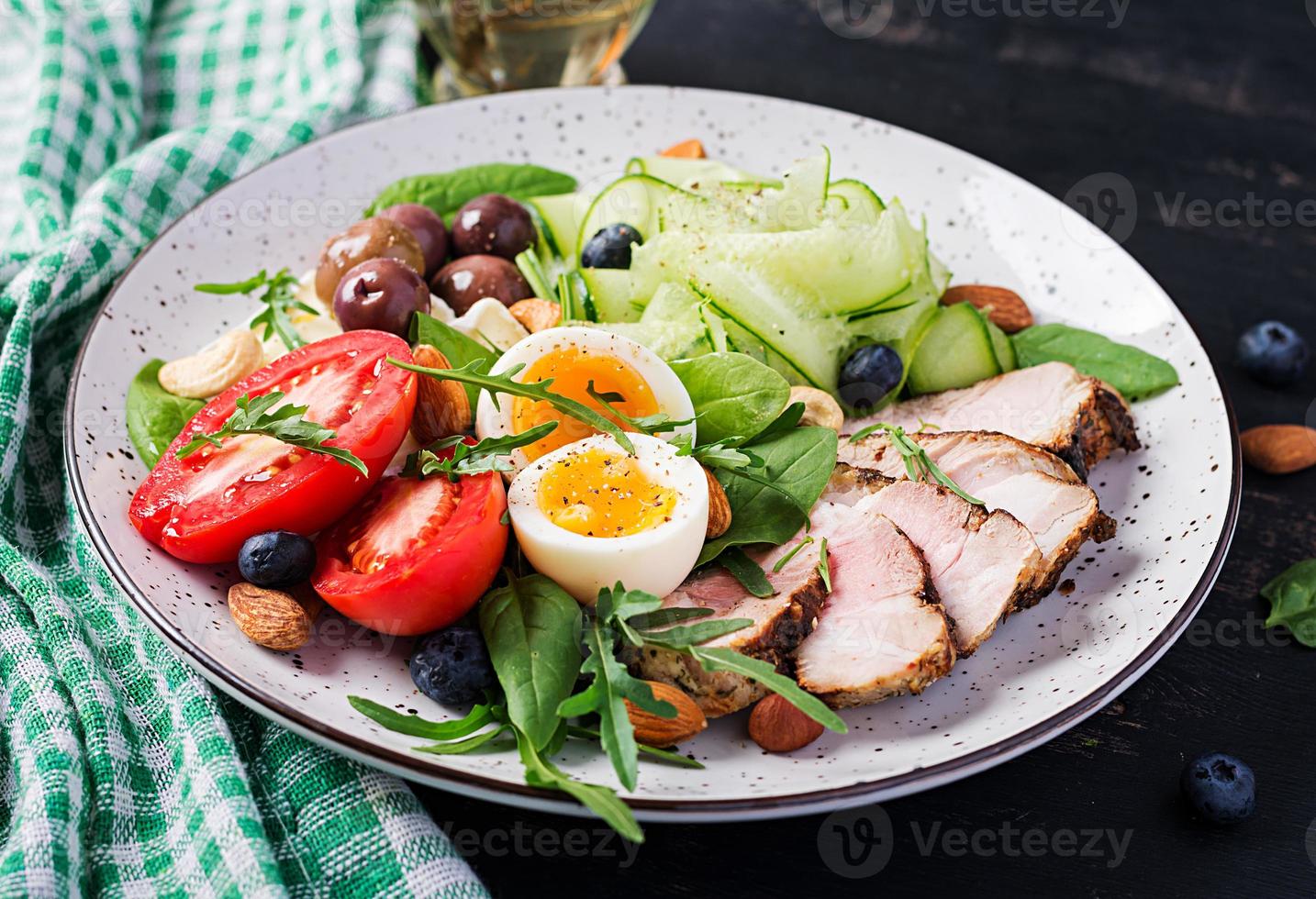Ketogenic diet. Keto brunch. Boiled egg, pork steak and olives, cucumber, spinach, brie cheese, nuts and tomato. photo
