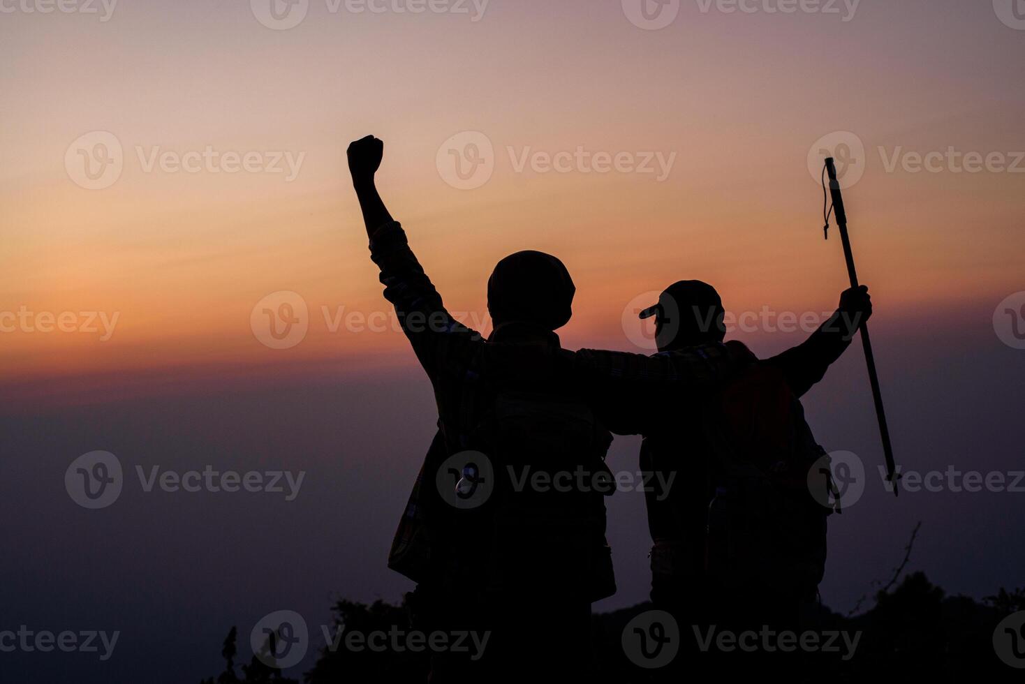 Silhouette of cheering hiking couple open arms to the sunrise sit on mountain photo