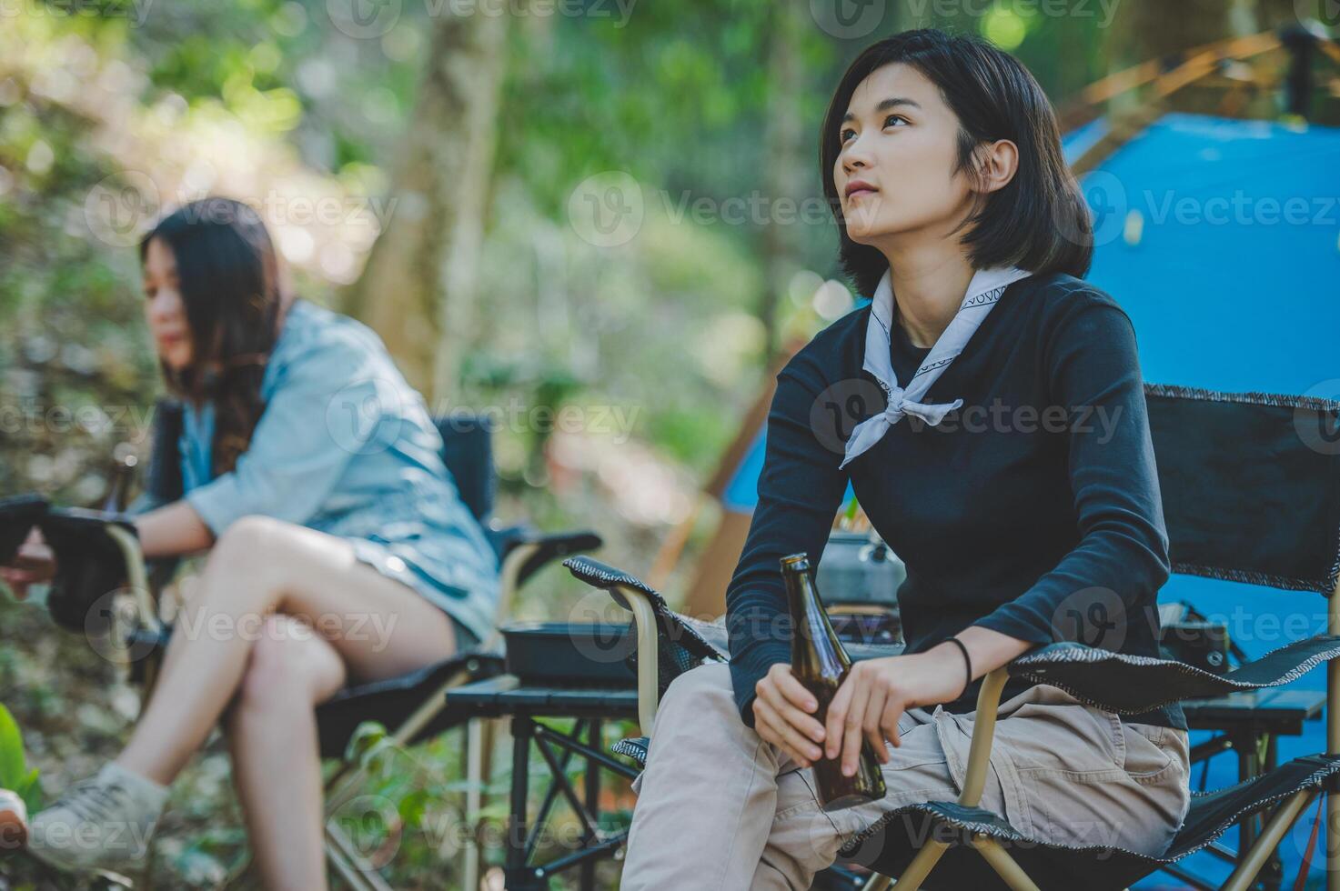 Young women sitting and drink beverage  front of camping tent photo