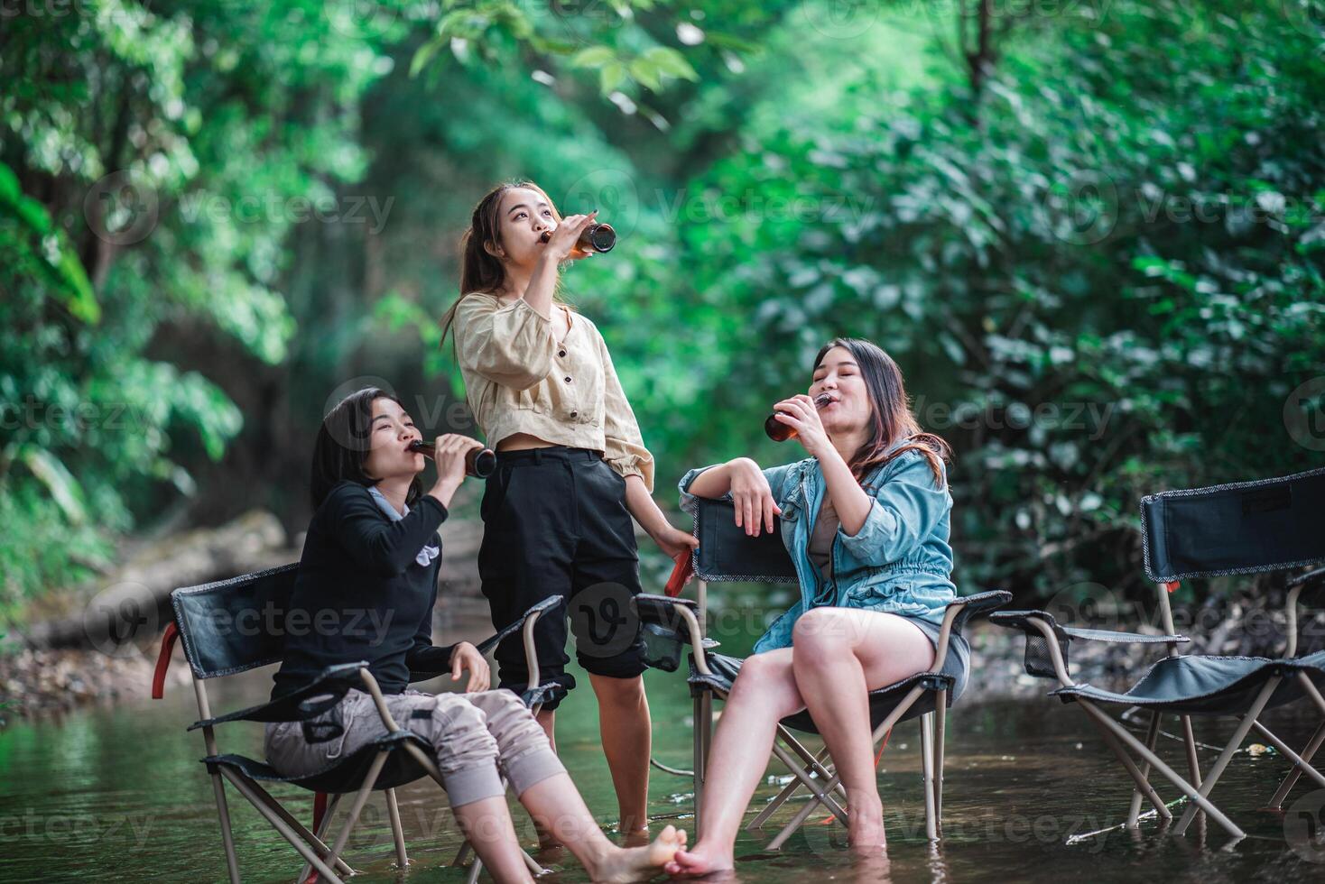 mujeres jóvenes sentadas y bebiendo bebidas mientras acampan en el bosque foto