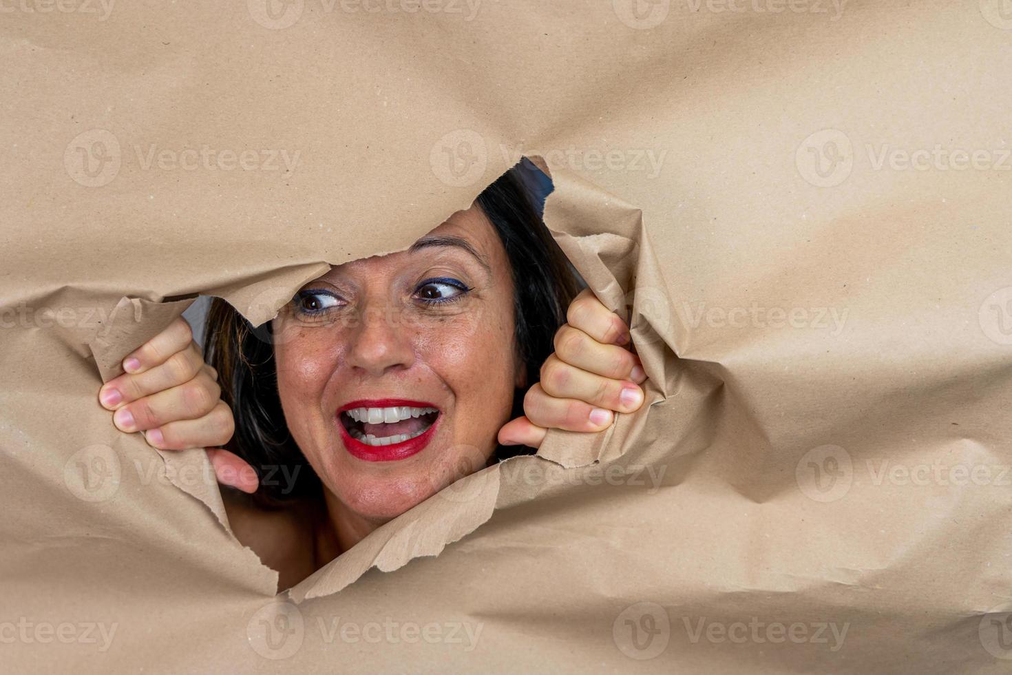 portrait of attractive mature woman is coming out of a hole in a sheet of paper photo