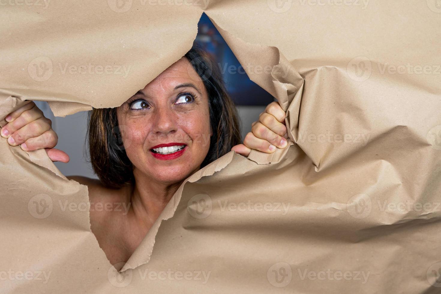 portrait of attractive mature woman is coming out of a hole in a sheet of paper photo