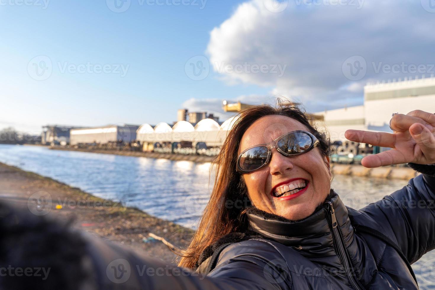 middle aged woman wearing winter clothes taking a selfie by a river photo