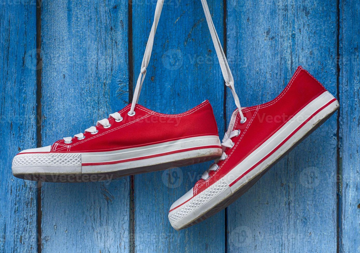 red sneakers hanging on a wooden blue background photo