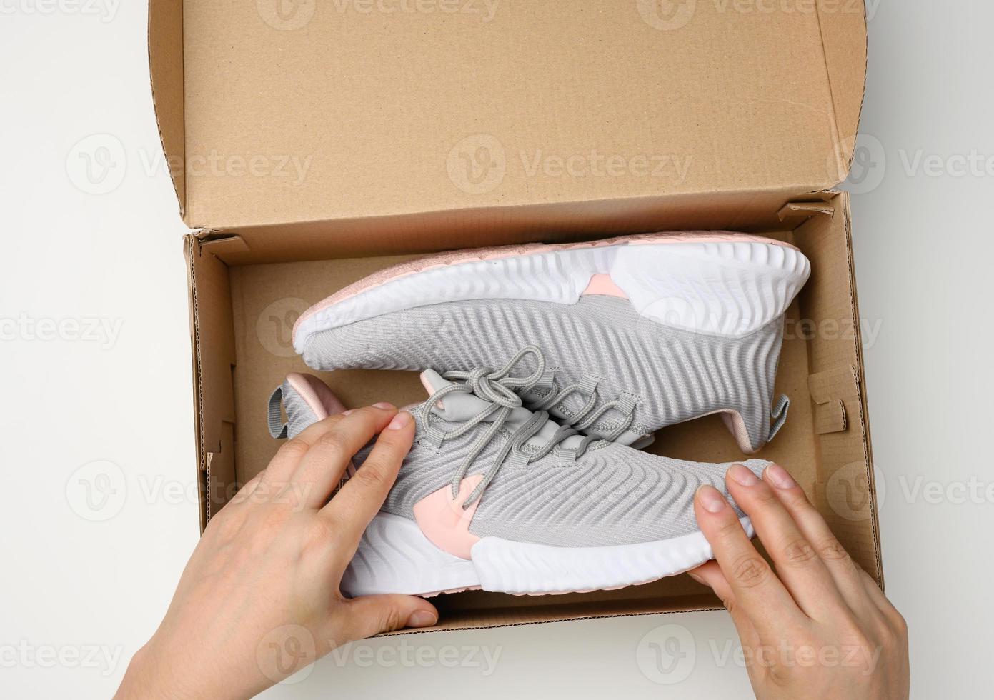two female hands are holding a brown cardboard box with gray sports sneakers on a white table, inspecting an online order photo