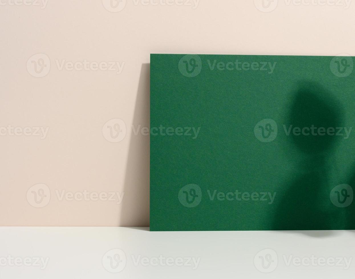 blank green cardboard sheet of paper with shadow on white table. Template for flyer photo