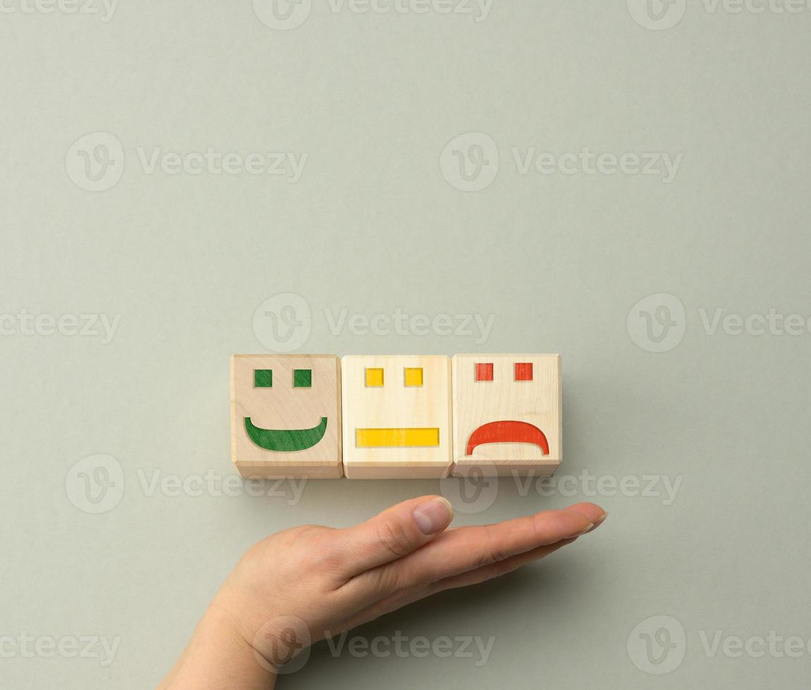 bloques de madera con diferentes emociones, desde la sonrisa hasta la tristeza y la mano de una mujer. concepto para evaluar la calidad de un producto o servicio foto