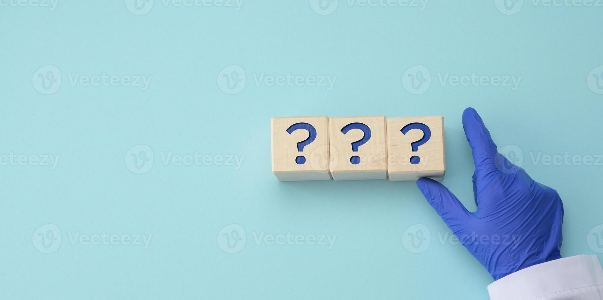 a hand in a blue medical glove holds cubes with question marks on a blue background. The concept of unknown, riddle, unanswered questions photo