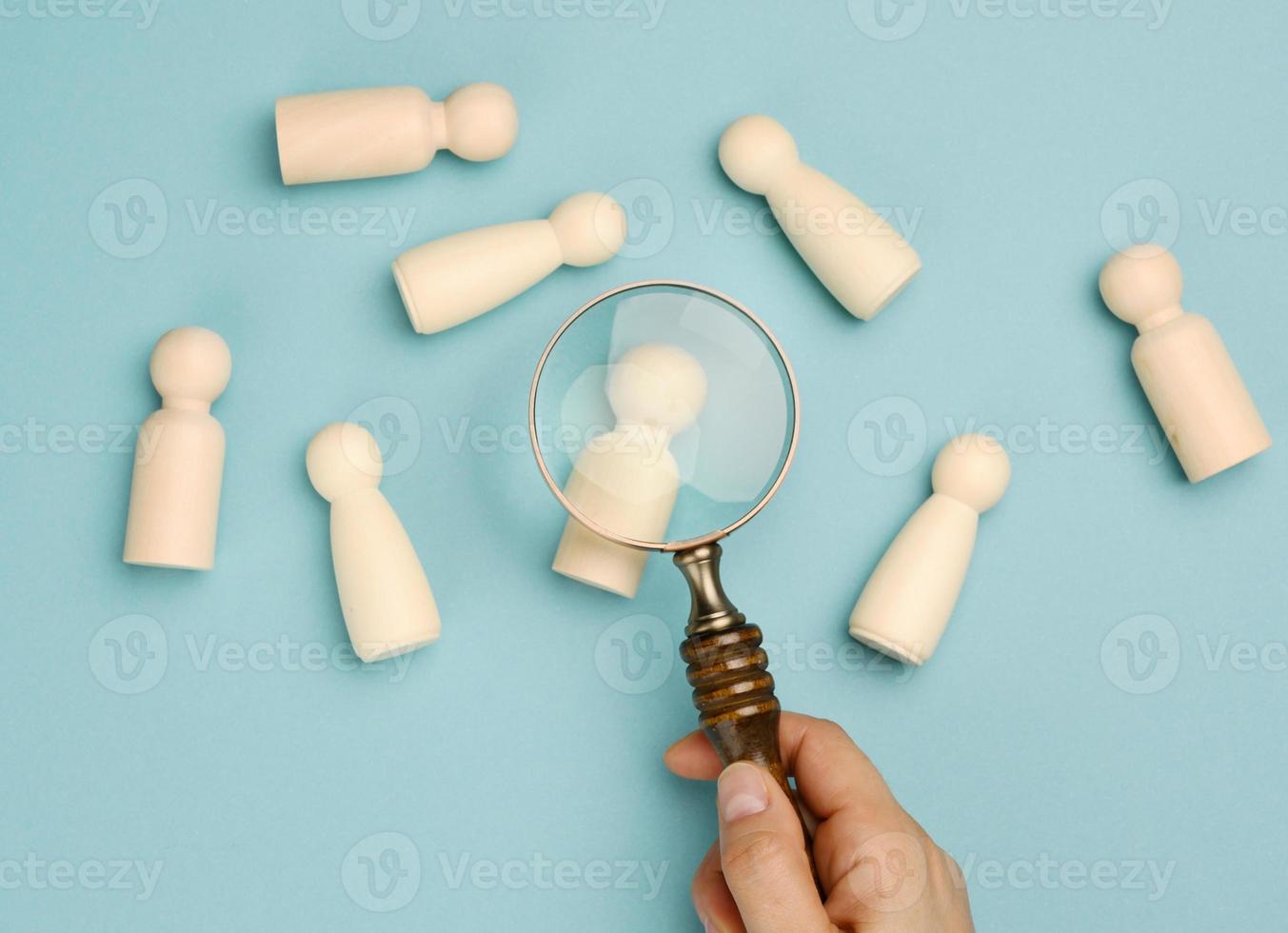 wooden men and a magnifying glass on a blue background. Recruitment concept, search for talented and capable employees, career growth, flat lay photo