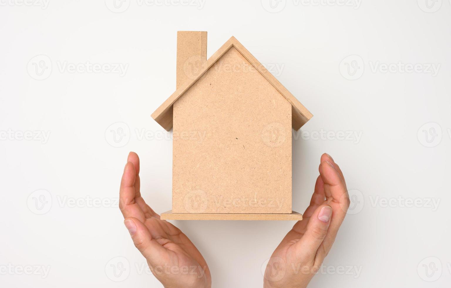 female hands folded to each other over a wooden miniature model house on a white background. Real estate insurance concept, photo