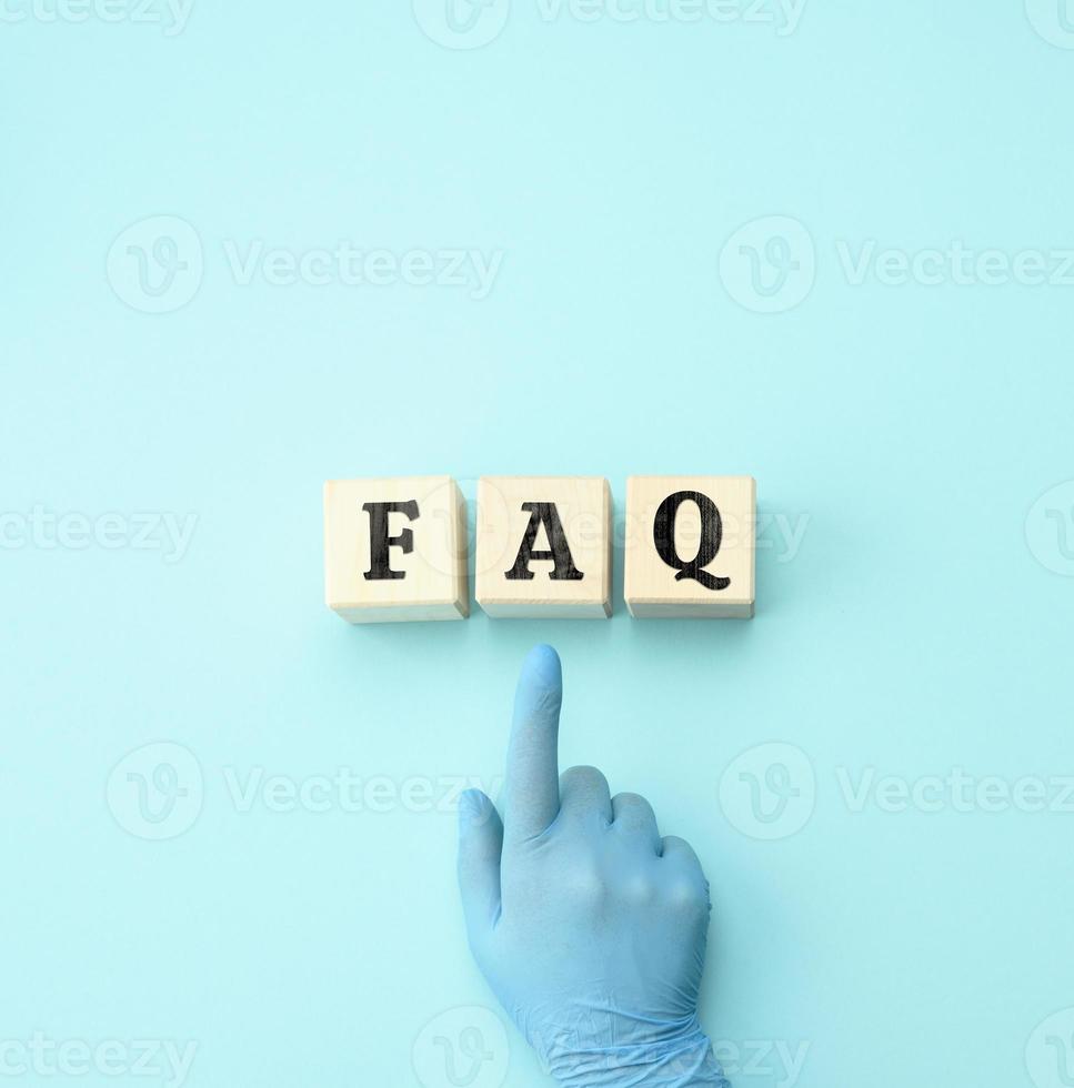 female hand in a blue latex glove points to wooden blocks with the inscription  FAQ frequently asked questions on a blue background photo