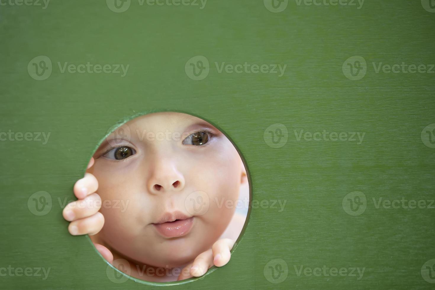 A little girl peeks through a hole. The face of a child in a circle. photo