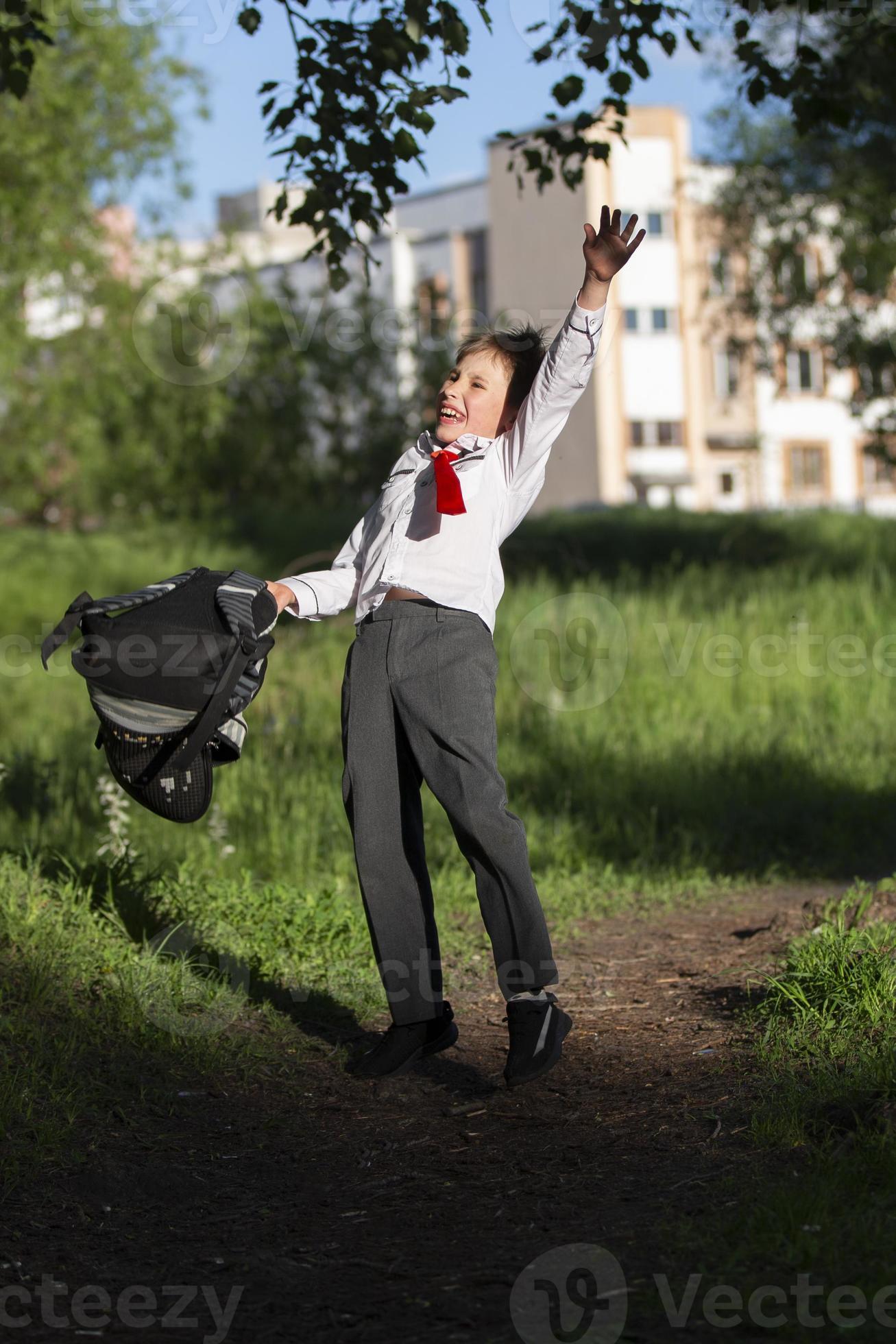 A happy schoolboy throws up his school backpack and rejoices at