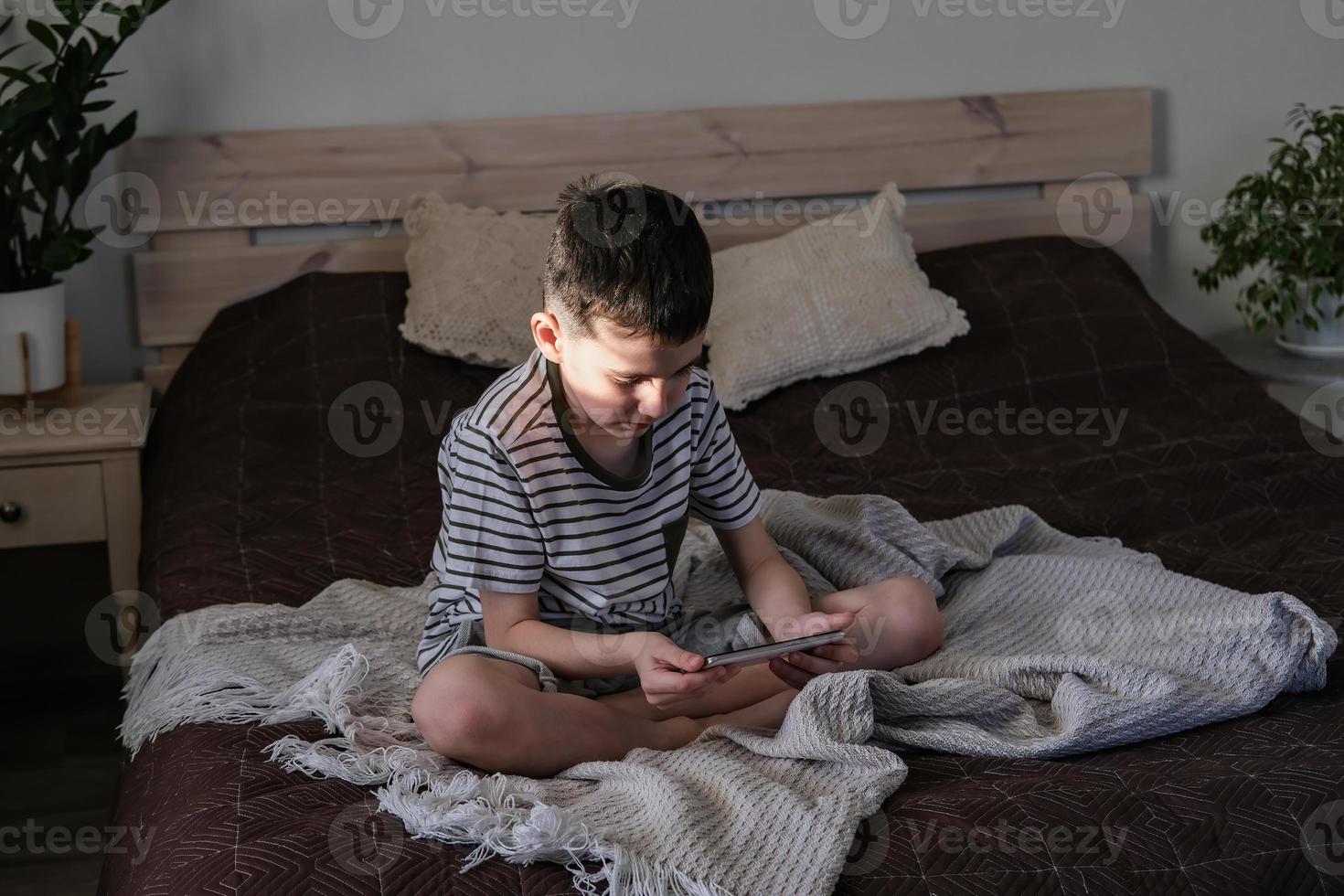 The boy sits on the bed and watches cartoons and videos on the smartphone photo