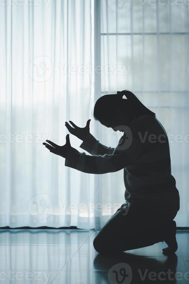 silhouette of woman kneeling and praying in modern church at sunset time. Female catholic prayer worship to God wish a better life in home at dawn with believe faith. concept of worshipers kneeling. photo