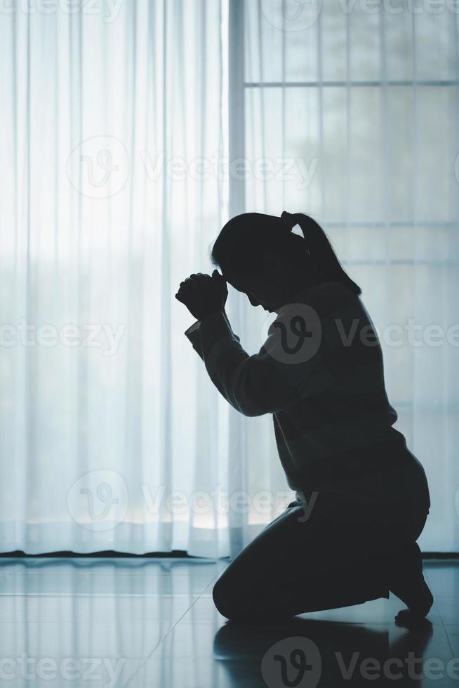 silhouette of woman kneeling and praying in modern church at sunset time. Female catholic prayer worship to God wish a better life in home at dawn with believe faith. concept of worshipers kneeling. photo